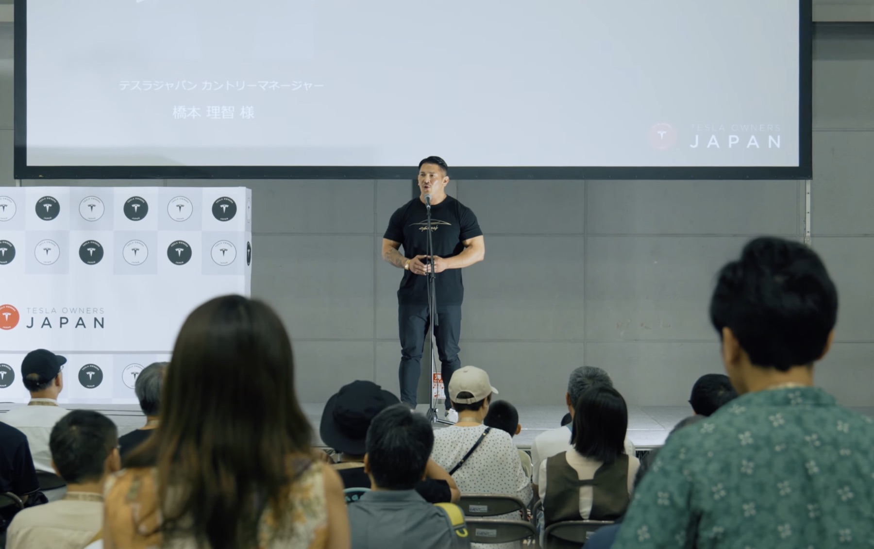 Tesla Japan President Mr. Hashimoto speaking on stage in 2025